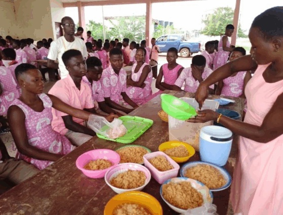 Senior high school students in uniform being served food from bowls during a school feeding session